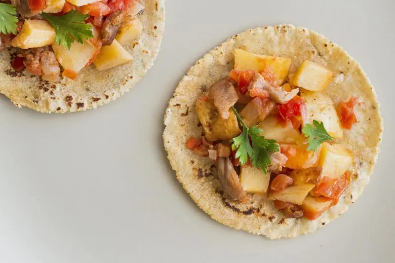 tacos de papa con chorizo servidos sobre tortillas de maiz con tomate y cilantro
