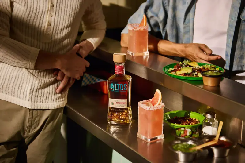 botella de tequila olmeca altos reposado con cocteles rosas y comida mexicana en barra