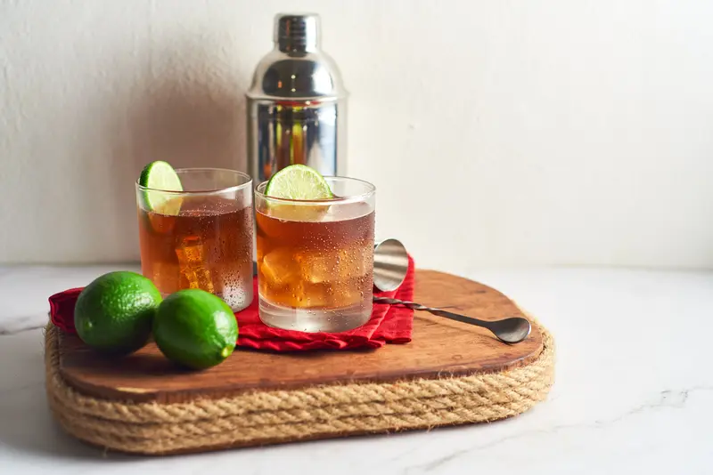 long Island iced tea with tequila and fresh lime Long Island iced tea cocktail with lime garnish and bar tools on wooden board