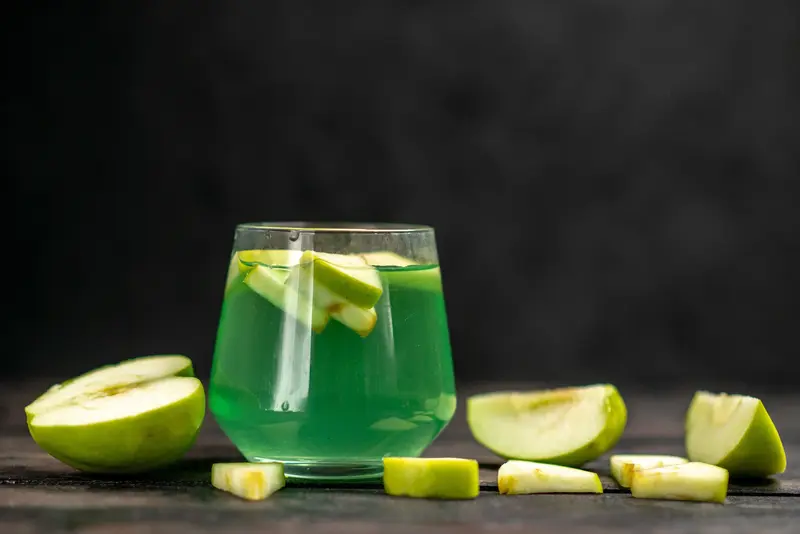 coctel de manzana verde con tequila Altos Plata copa con coctel de manzana verde y trozos de manzana Granny Smith sobre fondo oscuro