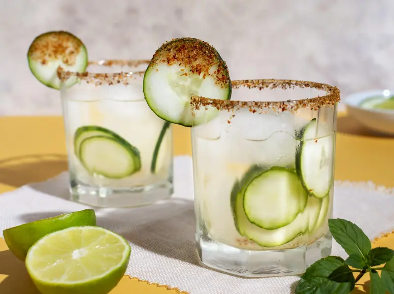 cócteles margarita de pepino con borde de chile y garnish de lima y pepino