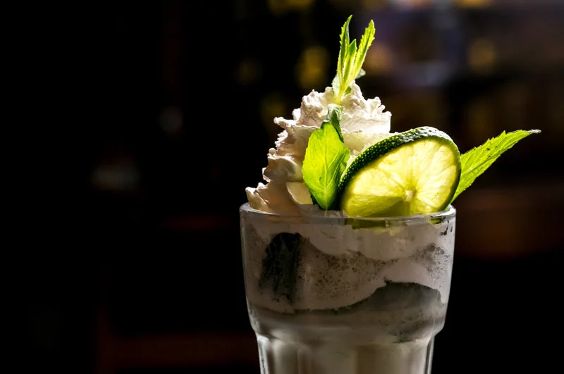 creamy tequila dessert cocktail with whipped cream lime slice and mint garnish