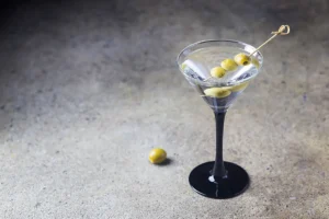 tequila dirty martini with green olives in martini glass on stone surface